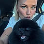 woman, dog, selfie, car, seatbelt, black_dog, pomeranian, fluffy, closeup, smile, playful, blonde_hair, makeup, tattoo, casual_clothing, daylight, vehicle_interior, happy, pet, portrait