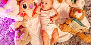 Jessica is registered to the contest to win money with this photo: baby, infant, plush_toys, teddy_bear, stuffed_animal, blanket, white_clothing, floor_rug, purple_rug, soft_texture, lying_down, cute, child, indoor, toy, cozy, relaxed, comfort, infant_clothing, playtime