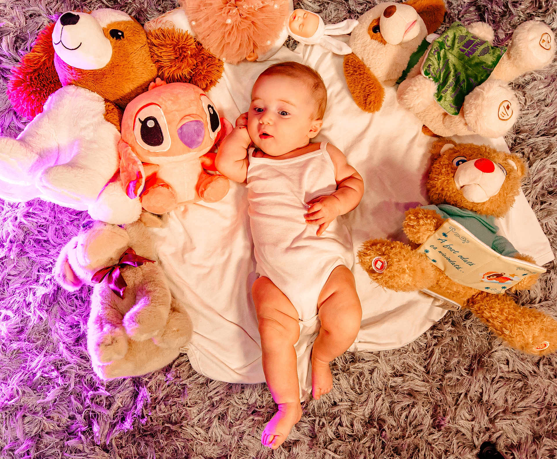 Jessica is registered to the contest to win money with this photo: baby, infant, plush_toys, teddy_bear, stuffed_animal, blanket, white_clothing, floor_rug, purple_rug, soft_texture, lying_down, cute, child, indoor, toy, cozy, relaxed, comfort, infant_clothing, playtime