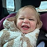 toddler, child, car_seat, jacket, fuzzy_clothing, seatbelt, indoor, face, expression, headrest, window, sky, hair, teeth, person, portrait, car_interior, warm_clothing, closeup, baby