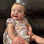 Remi joined the competition — help win amazing prizes! baby, child, infant, smiling, sitting, dress, floral_pattern, hair_bows, couch, leather, indoor, cute, happy, person, young_child, skin, hand, face, portrait, comfort