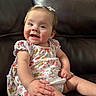 baby, child, infant, smiling, sitting, dress, floral_pattern, hair_bows, couch, leather, indoor, cute, happy, person, young_child, skin, hand, face, portrait, comfort