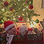 Charlie is registered to the contest to win money with this photo: baby, christmas_tree, ornaments, lights, gift_box, plush_toy, santa_hat, holiday, festive, decorations, teddy_bear, child, indoors, floor, wrapped_gift, seasonal, cute, holiday_spirit, celebration, smiling