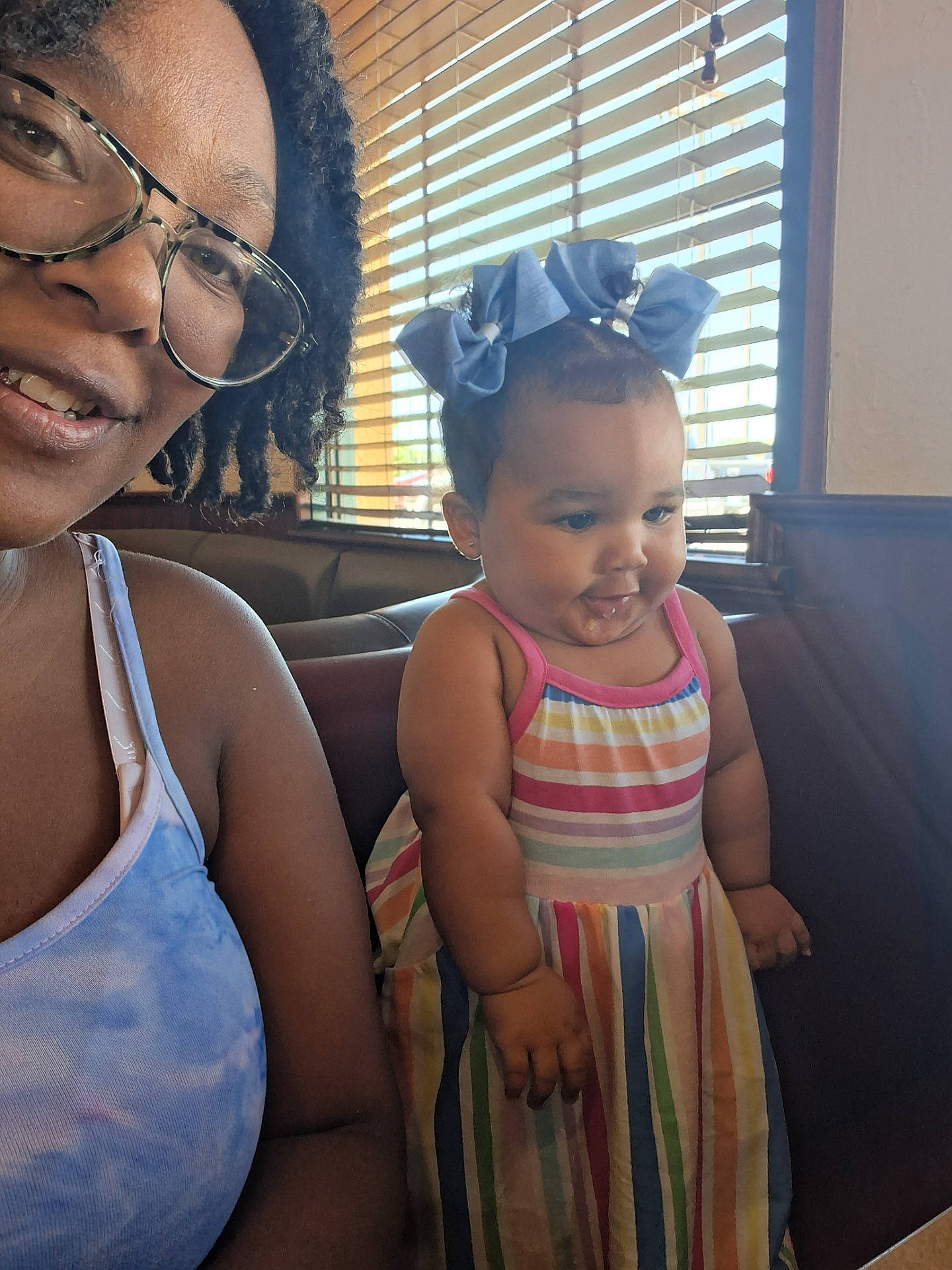 Kea'Loni joined the competition — help win amazing prizes! blinds, child, colorful, dress, face, glasses, hair_bows, happy, indoor, light, person, portrait, restaurant, sitting, skin, smile, table, toddler, window, woman