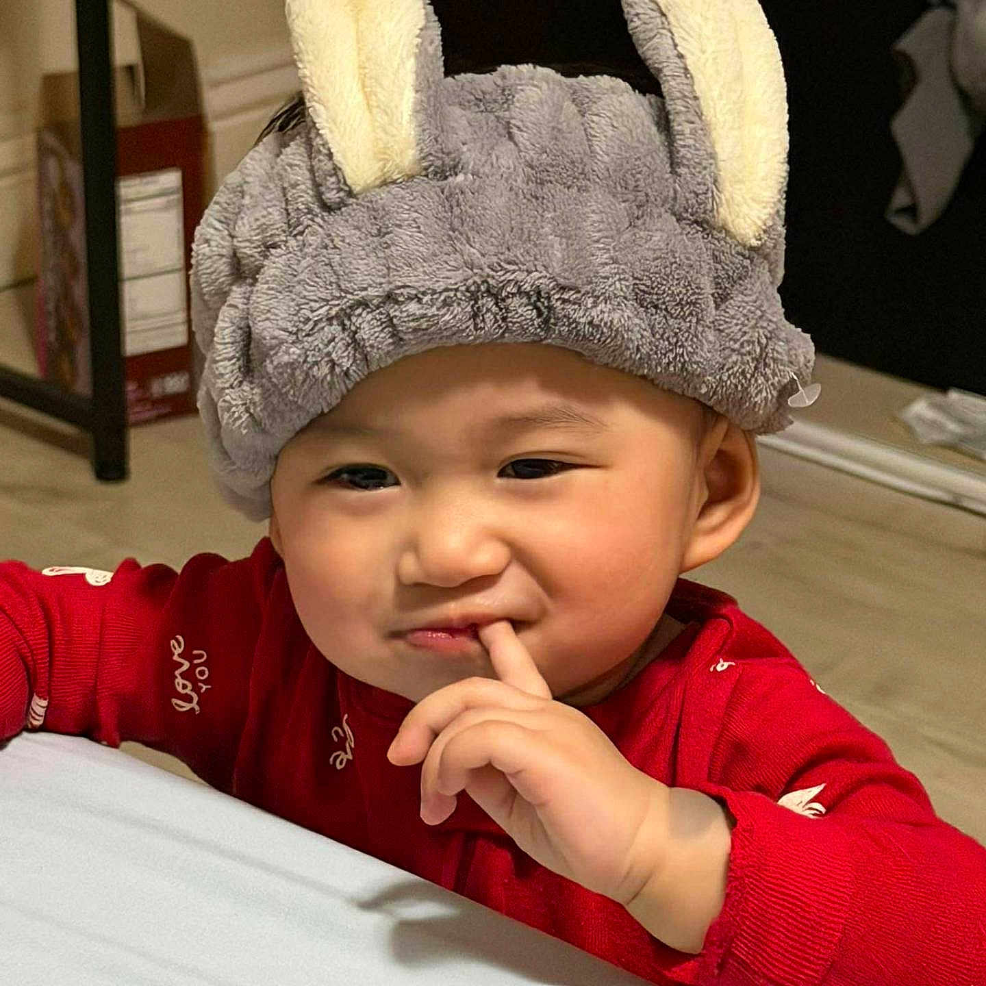 Celine Duyen Lam is registered to the contest to win money with this photo: baby, child, portrait, smiling, bunny_hat, red_outfit, indoor, bedroom, cozy, closeup, face, hand, finger, cute, infant, sitting, soft_hat, fuzzy, playful, photography