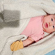 Celine joined the competition — help win amazing prizes! baby, blanket, pink_shirt, yellow_mitten, infant, cozy, soft_texture, lying_down, face, skin, portrait, cute, newborn, indoors, warm, child, sleepwear, bed, comfort, resting