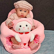 Celine is registered to the contest to win money with this photo: baby, child, pink, plush_chair, cat_shape, soft_toys, cozy_clothing, hat, indoors, feet, cute, adorable, sitting, portrait, expression, face, furniture, background, comfort, infant