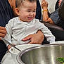 adult, baby, bowl, bracelet, casual, child, clothing, family, food, hand, indoor, metal_bowl, person, phone, relaxed, seated, smiling, spoon, table, vegetables