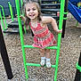 child, girl, playground, play_equipment, smiling, happy, outdoor, wood_chips, green_bars, dress, shoes, socks, daylight, fun, recreation, climbing, park, young_child, casual_clothing, joy