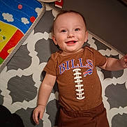 Paxtyn joined the competition — help win amazing prizes! baby, infant, child, smiling, lying_down, onesie, bills_logo, football_design, play_mat, rug, hat, arm, hand, eyes, teeth, happy, indoor, portrait, blanket, floor