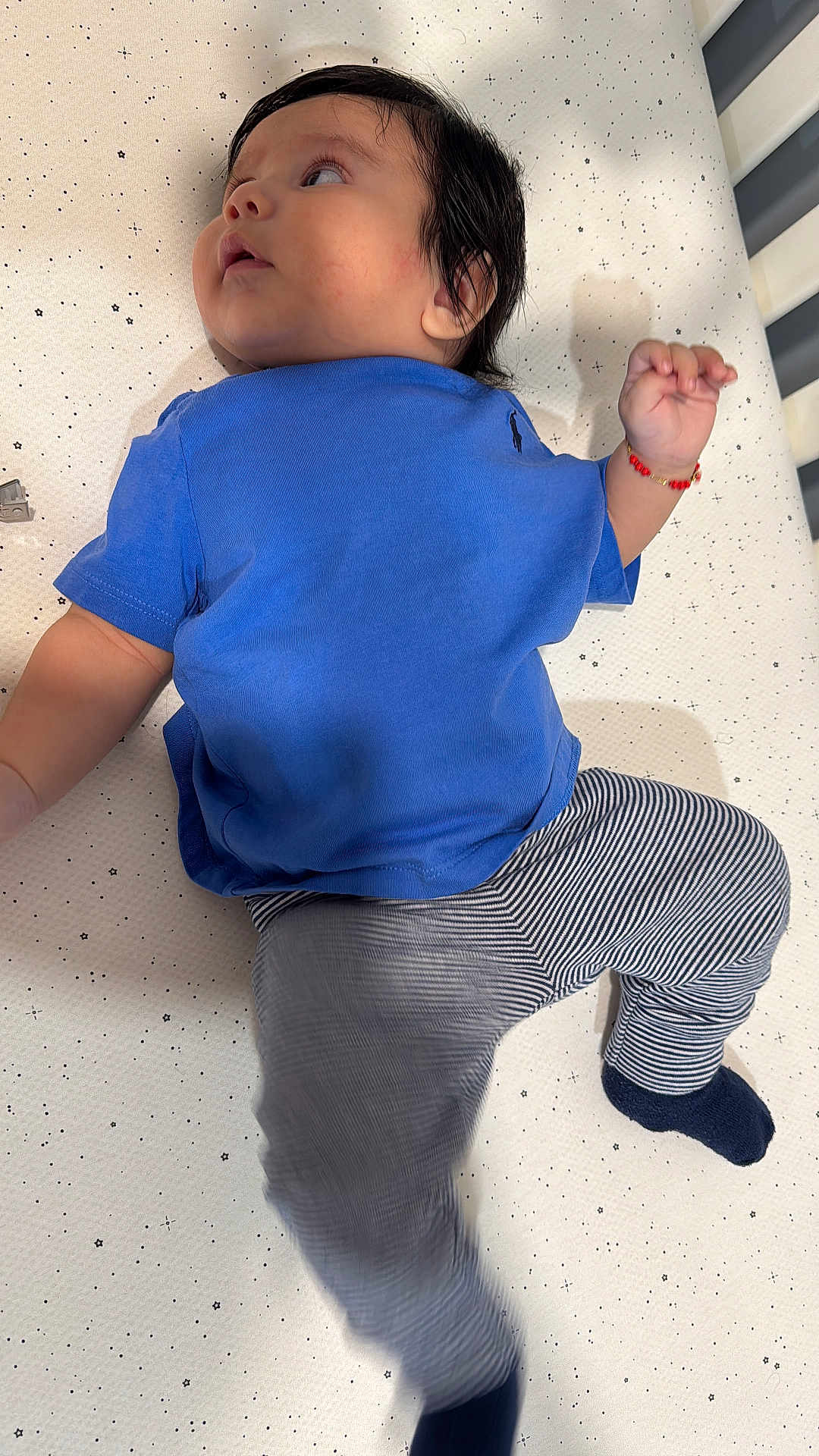 Leo Cuji joined the competition — help win amazing prizes! baby, child, blue_shirt, striped_pants, bracelet, crib, mattress, stars_pattern, lying_down, motion_blur, curious, infant, clothing, footwear, sock, indoors, person, young_child, cute, portrait