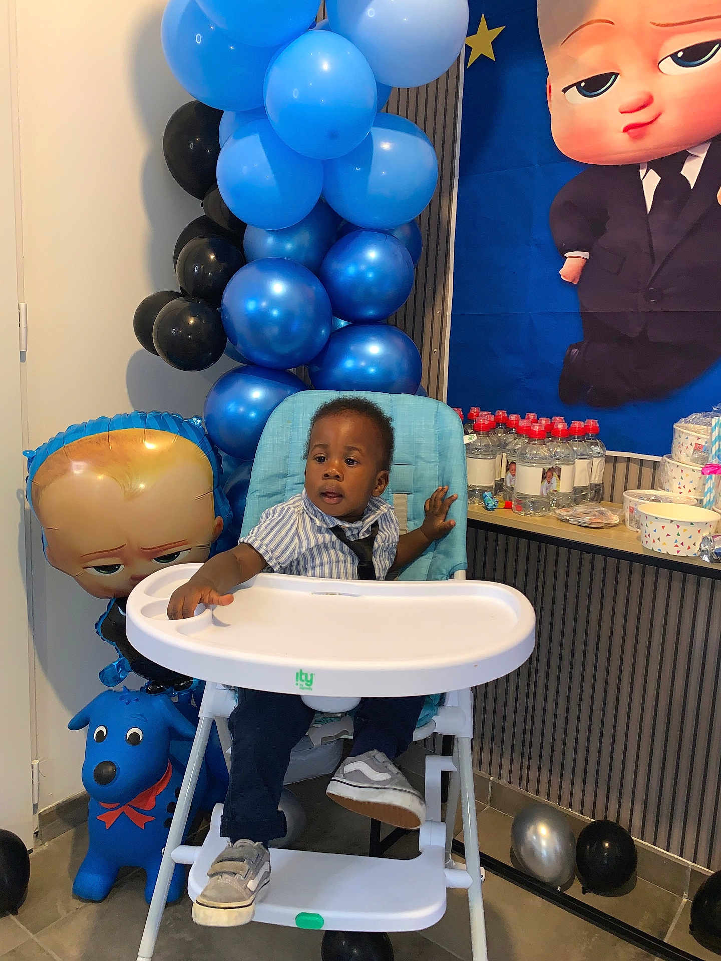 Willan a rejoint le concours — aidez-le/la à gagner de superbes lots ! toddler, high_chair, balloons, party, blue, black, child, shirt, tie, shoes, floor, table, bottle, decoration, plastic, indoor, celebration, cartoon, toy, curious