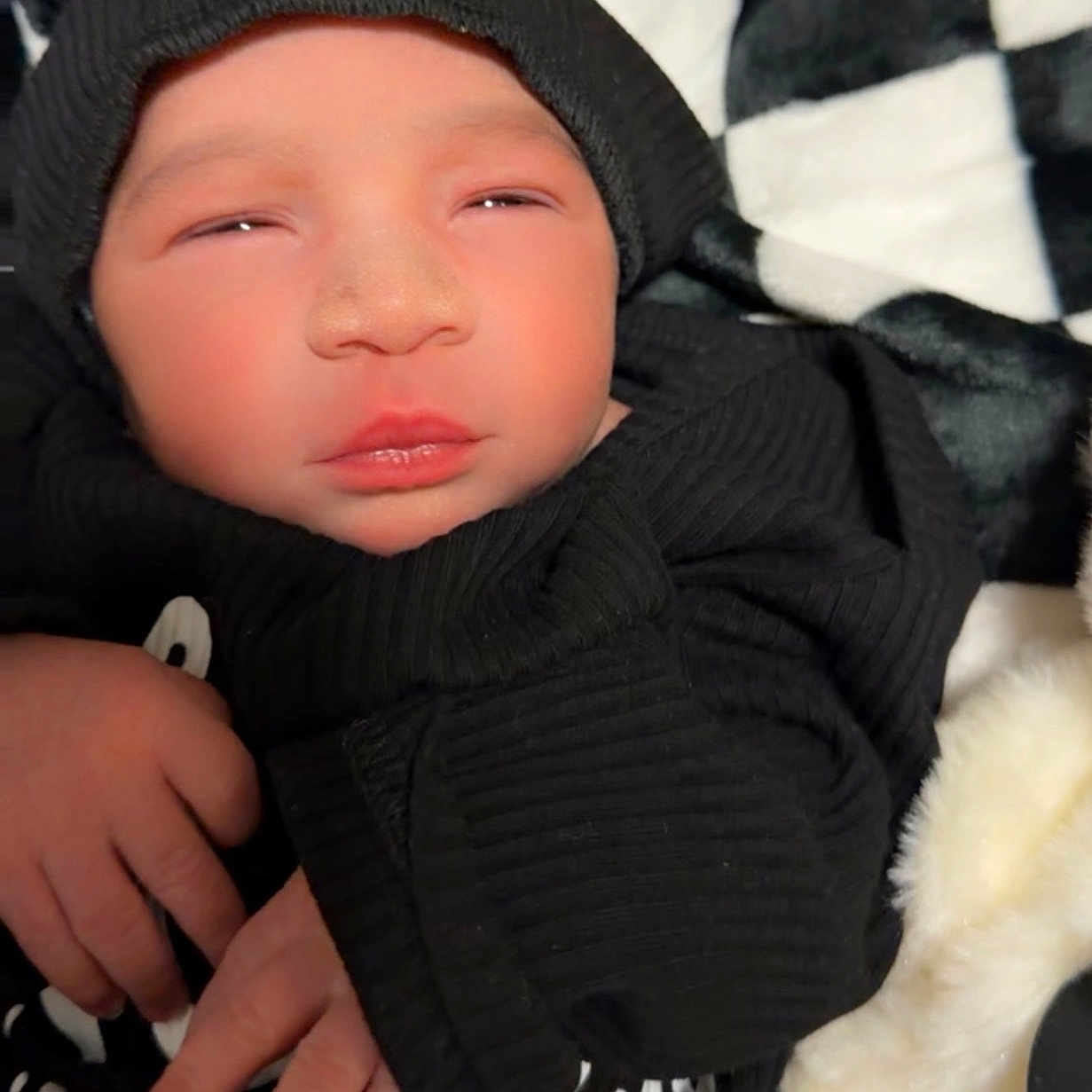 Latrell joined the competition — help win amazing prizes! baby, black_hoodie, blanket, checkered_pattern, child, clothing, cozy, cute, face, hand, hood, indoors, infant, newborn, portrait, resting, sleepy, soft_texture, toddler, young
