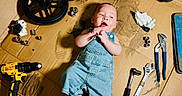 Albert is registered to the contest to win money with this photo: baby, denim_overalls, cardboard, tools, wrench, pliers, drill, wheel, hardware, mechanic, child, floor, curious, playful, indoor, hand_tool, foot, face, small_tool, exploration