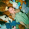 baby, stuffed_animals, plush_toys, blanket, bear, bunny, dog_toy, elephant_toy, blue_toy, green_blanket, infant, child, soft_toys, cute, cozy, indoor, portrait, sleepwear, comfort, snuggle