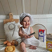 Marlow a rejoint le concours — aidez-le/la à gagner de superbes lots ! apron, baby, baking, chef_hat, child, cooking, countertop, cute, eggs, flour, food, happy, indoors, kitchen, messy, pastry, person, playful, smiling, whisk