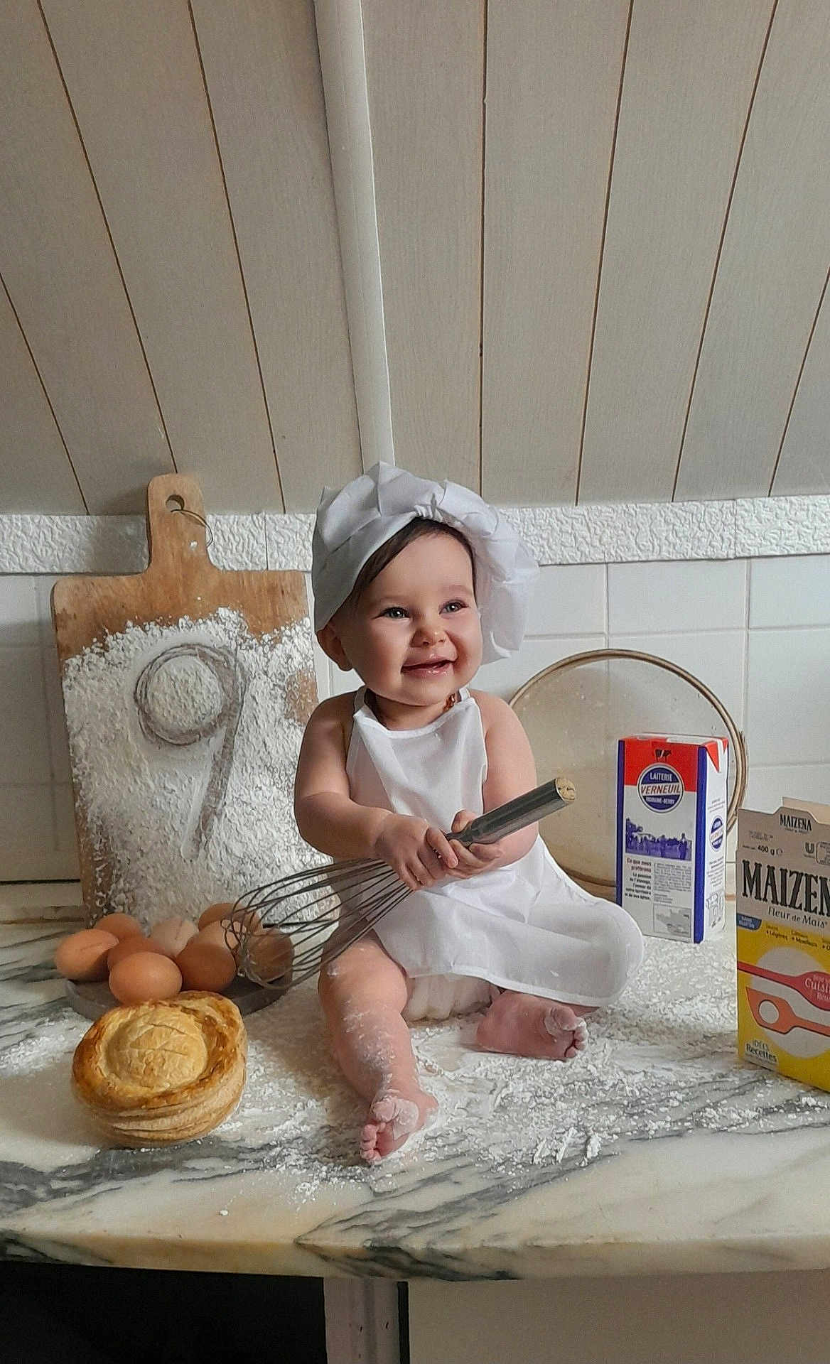 Marlow a rejoint le concours — aidez-le/la à gagner de superbes lots ! apron, baby, baking, chef_hat, child, cooking, countertop, cute, eggs, flour, food, happy, indoors, kitchen, messy, pastry, person, playful, smiling, whisk