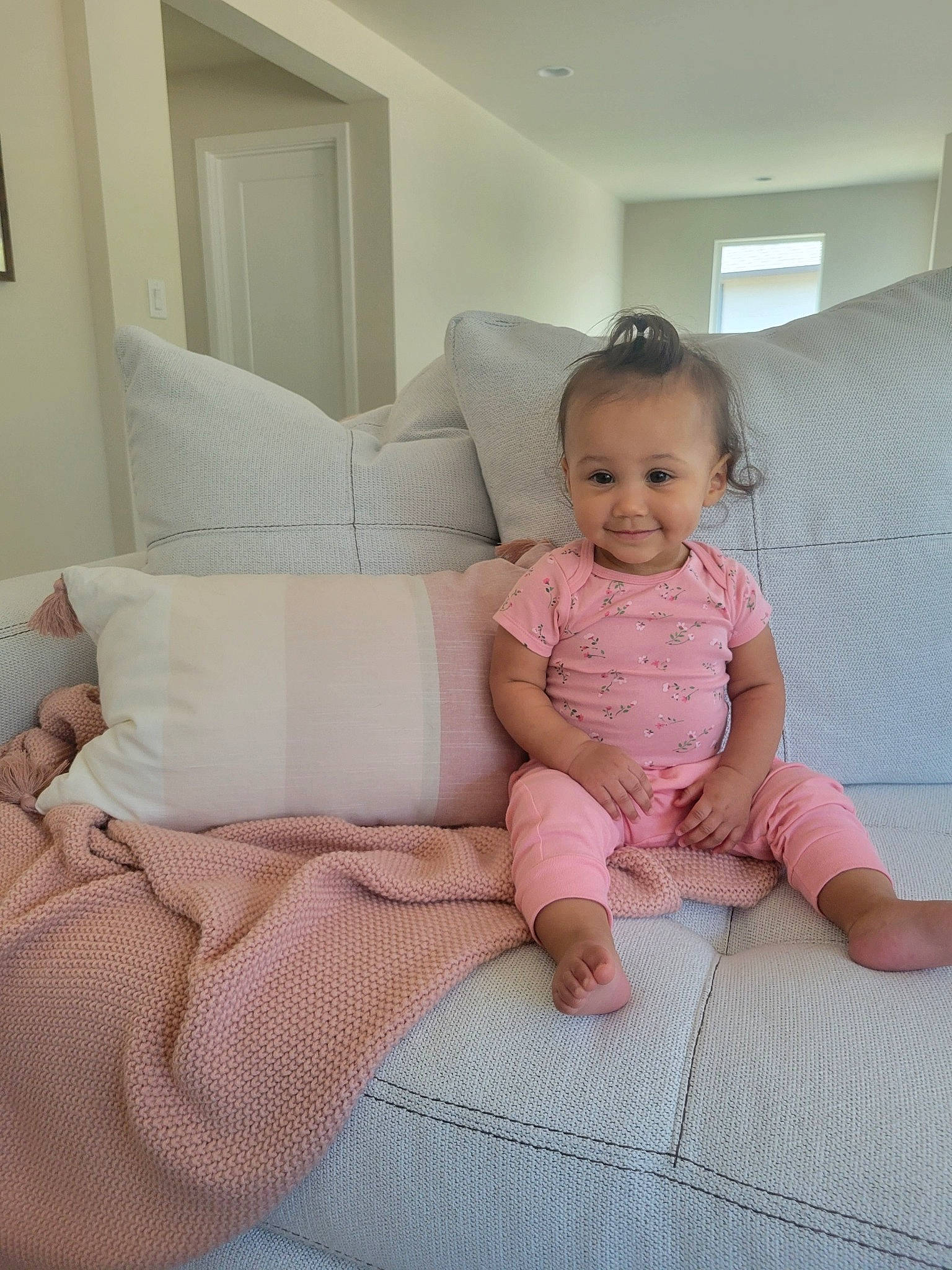 Elliana is registered to the contest to win money with this photo: baby, baby_toddler_clothing, bedding, child, comfort, couch, eye, floor, flooring, foot, human_leg, joy, linens, person, pink, room, sitting, sleeve, t_shirt, throw_pillow