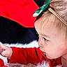 toddler, child, baby, face, hand, red_clothing, headband, green_bow, plush_toy, santa_claus, holiday, christmas, curious, indoor, soft_texture, close_up, portrait, candid, cute, festive