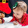 baby, child, plush_toy, moose, red_clothing, green_clothing, headband, christmas_stocking, holiday_theme, fluffy_rug, toy, portrait, curious, indoor, cute, smiling, festive, holiday_decor, person, closeup