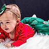 baby, child, infant, red_clothing, green_skirt, headband, bow, fluffy_surface, white_texture, smiling, portrait, cute, holiday_theme, indoor, studio, young_child, lying_down, happy, face, person