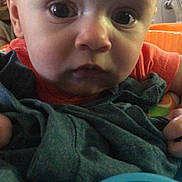 Jennsyn is registered to the contest to win money with this photo: baby, face, close_up, toy, blue, blanket, curious, child, infant, clothing, orange, indoor, person, head, eyes, hand, expression, young, portrait, holding