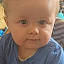 Noah is registered to the contest to win money with this photo: baby, child, curly_hair, blue_shirt, hands, food, crumbs, indoor, face, eyes, cute, portrait, table, skin, expression, infant, person, young_child, closeup, casual