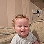 toddler, child, smiling, curly_hair, indoor, couch, beige, shirt, happy, face, person, plush, home_interior, wallpaper, power_outlet, light, seated, cute, skin, baby