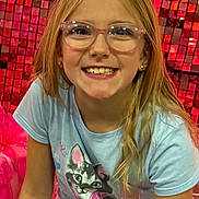 Cassidy is registered to the contest to win money with this photo: child, girl, smiling, glasses, long_hair, tshirt, cat_print, cast, arm_cast, jeans, seated, red_background, mosaic_wall, happy, portrait, indoor, casual_clothing, earrings, person, youth