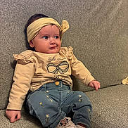 Lina participe au concours pour gagner de l'argent avec cette photo : baby, infant, headband, bow, sitting, sofa, couch, clothing, jeans, embroidered, shoes, minnie_mouse, hand, face, eyes, cheeks, portrait, indoor, text_on_shirt, soft_furnishing