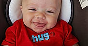 Brently is registered to the contest to win money with this photo: baby, smiling, red_shirt, blanket, toy, face, child, infant, happy, cushion, seat, closeup, cute, person, indoor, hand, head, expression, comfort, playtime