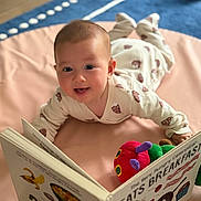 Azelia is registered to the contest to win money with this photo: baby, child, pajamas, book, reading, toy, plush, floor, mat, indoor, smiling, cute, infant, play, early_learning, colorful, soft, happy, portrait, cozy