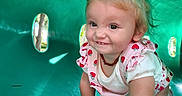 Hartley joined the competition — help win amazing prizes! baby, child, clothing, crawling, cute, face, green_tunnel, hair, hand, happy, necklace, outdoor, person, pink, play, playground, skin, smiling, sunlight, toddler