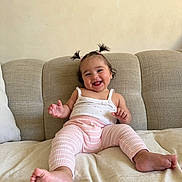 Isée participe au concours pour gagner de l'argent avec cette photo : baby, child, smiling, happy, pigtails, pink_pants, white_tank_top, couch, beige, indoor, person, cute, infant, small_hands, barefoot, plush, relaxed, portrait, sitting, home