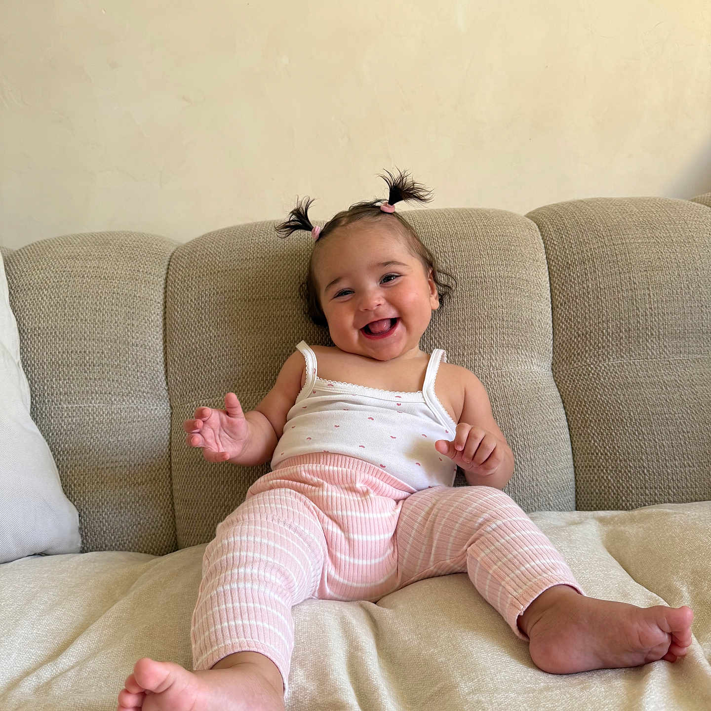 Isée participe au concours pour gagner de l'argent avec cette photo : baby, barefoot, beige, child, couch, cute, happy, home, indoor, infant, person, pigtails, pink_pants, plush, portrait, relaxed, sitting, small_hands, smiling, white_tank_top