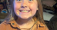 Blakely joined the competition — help win amazing prizes! child, smiling, face, brown_jacket, corduroy, blonde_hair, indoors, portrait, happy, wide_eyes, person, girl, buttoned_jacket, long_hair, vintage_decor, wooden_wall, earrings, casual_clothing, expression, warm_lighting