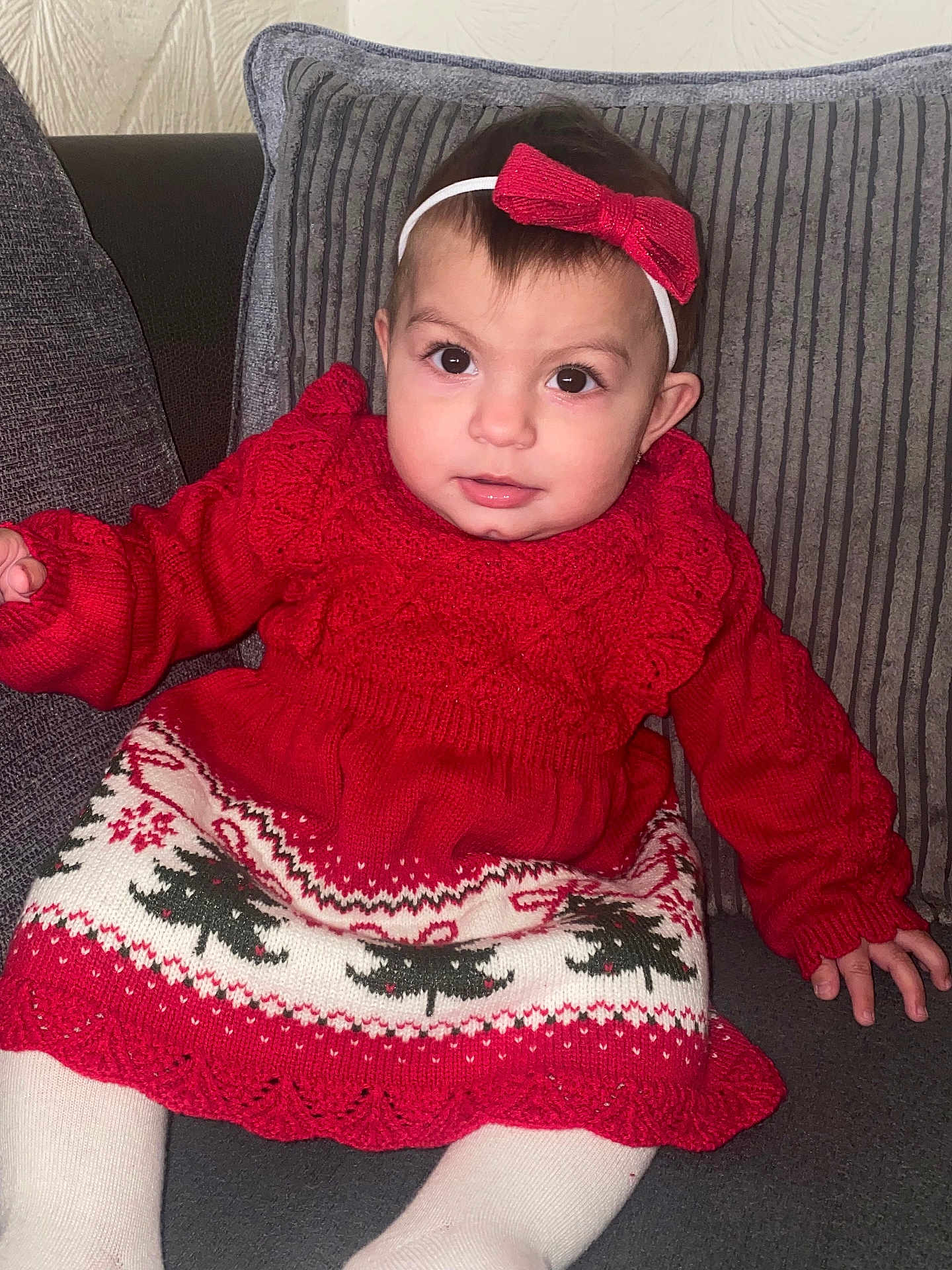 Ashley joined the competition — help win amazing prizes! baby, child, infant, red_sweater, christmas_dress, headband, red_bow, couch, cushion, white_tights, indoors, portrait, cute, smiling, holiday, festive, seated, looking_at_camera, face, person