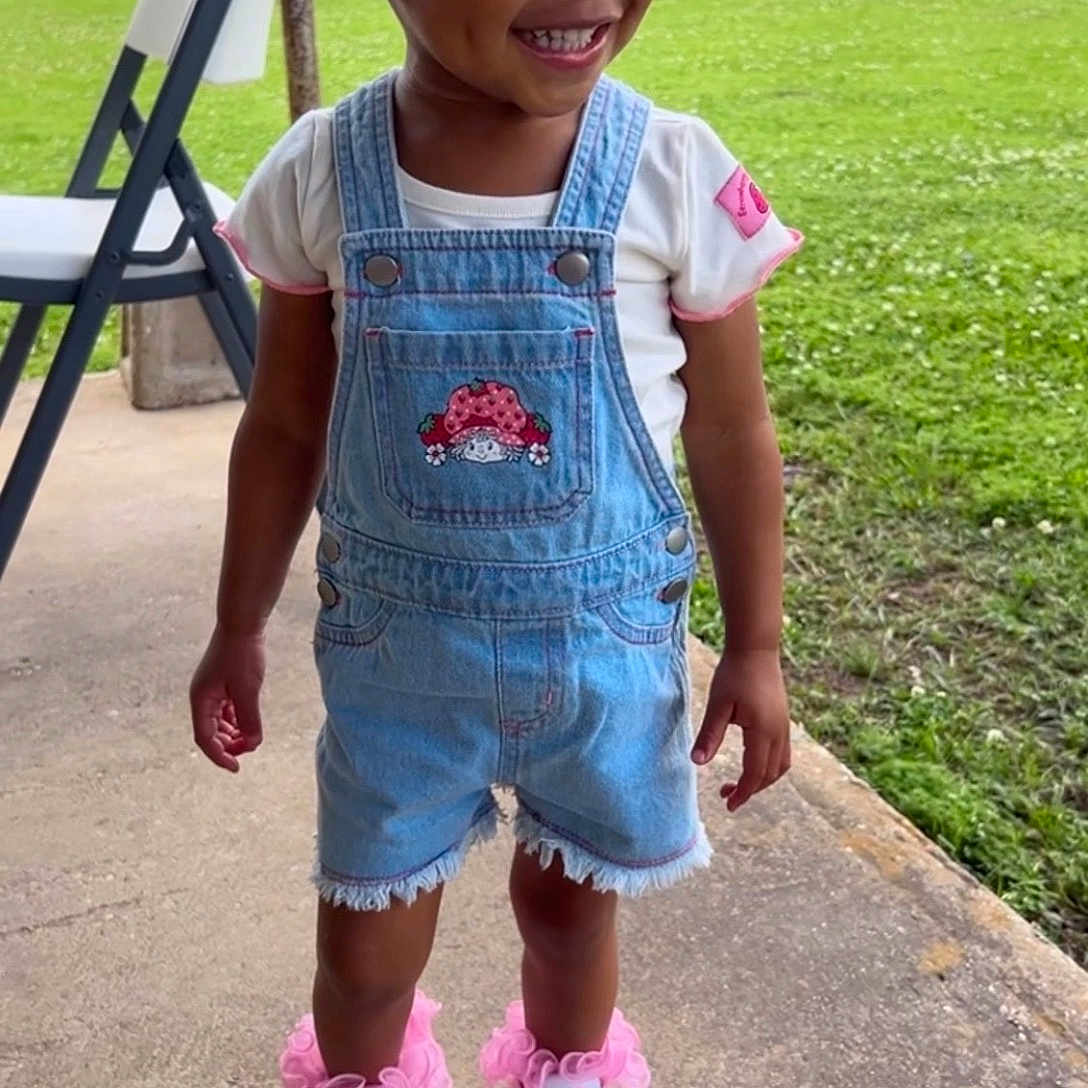 Alayla joined the competition — help win amazing prizes! toddler, child, smiling, denim_overalls, white_tshirt, pink_bows, outdoor, grass, concrete_path, folding_chair, happy, cute_shoes, pink_flowers, shorts, person, portrait, casual_clothing, daytime, nature, playful