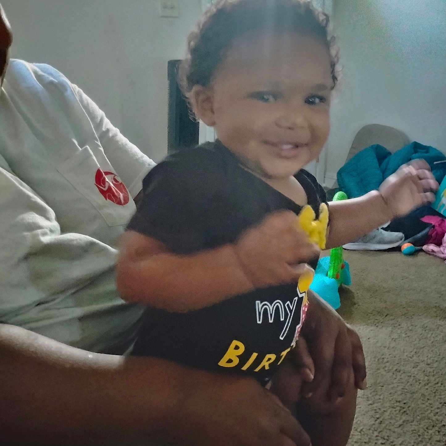 Eddonia Smith joined the competition — help win amazing prizes! adult, baby, black_shirt, carpet, casual, child, clothing, curly_hair, family, hand, happy, home, indoor, living_room, person, playful, seated, smiling, toddler, toy