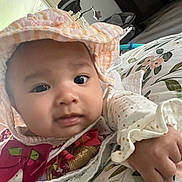 Adriana is registered to the contest to win money with this photo: baby, infant, child, bonnet, frilly_clothing, portrait, close_up, face, eyes, looking_at_camera, plush_toy, blanket, floral_pattern, bed, indoor, home, sitting, hand, cozy, photography