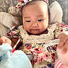 Adriana is registered to the contest to win money with this photo: baby, child, infant, portrait, face, headband, floral_dress, patterned_clothing, smiling, sitting, indoor, blanket, cushion, bottle, feeding, adult_hand, close_up, soft_lighting, home, family