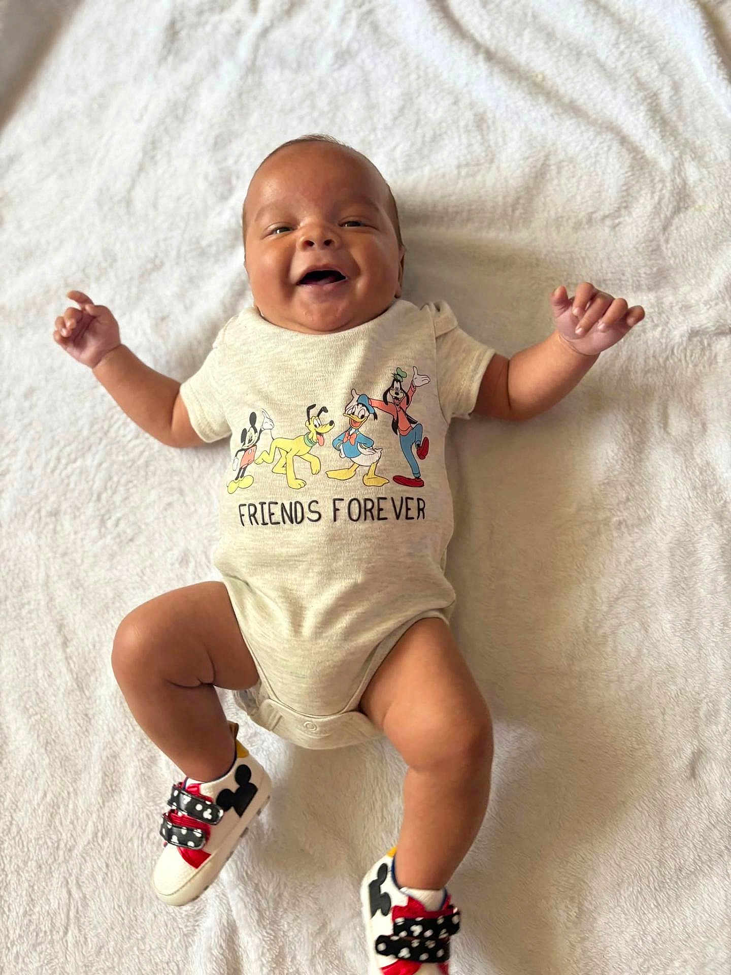 Mi'Zeir is registered to the contest to win money with this photo: baby, infant, smiling, onesie, disney, mickey_mouse, donald_duck, goofy, pluto, shoes, white_blanket, happy, cute, child, portrait, lying_down, feet, clothing, baby_shoes, friends_forever