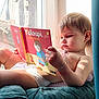 André participe au concours pour gagner de l'argent avec cette photo : baby, book, bracelet, child, cushion, diaper, expression, face, hand, indoor, necklace, pillow, portrait, reading, roof, storybook, sunlight, toddler, window, windowsill