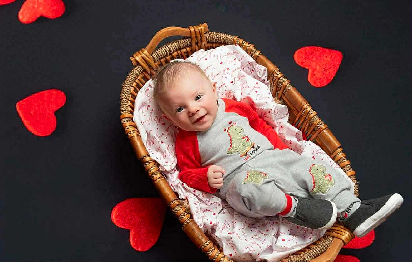 Zayden is registered to the contest to win money with this photo: baby, infant, basket, blanket, heart_shapes, valentine_theme, smile, portrait, wicker, pajamas, dinosaur_motif, sneakers, black_background, red_hearts, lying_down, cute, studio_photo, happy, cozy, child