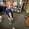 Paislee is registered to the contest to win money with this photo: child, girl, indoor, carpet, clothing, blue_shirt, patterned_pants, hair_bun, smile, face, socks, crocs, floor, shelf, household_items, doorway, mat, person, room, casual
