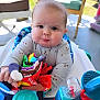 baby, child, toy, high_chair, colorful, soft_toy, indoor, pout, curious, plastic_toys, blue, turquoise, seat, clothing, long_sleeve, cute, face, hands, infant, person