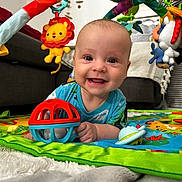 Gioele participe au concours pour gagner de l'argent avec cette photo : baby, smiling, toy, play_mat, indoor, child, colorful, plush_toy, happy, crawling, living_room, fabric, person, cute, infant, play_gym, face, blue_shirt, carpet, close_up