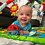 baby, smiling, toy, play_mat, indoor, child, colorful, plush_toy, happy, crawling, living_room, fabric, person, cute, infant, play_gym, face, blue_shirt, carpet, close_up