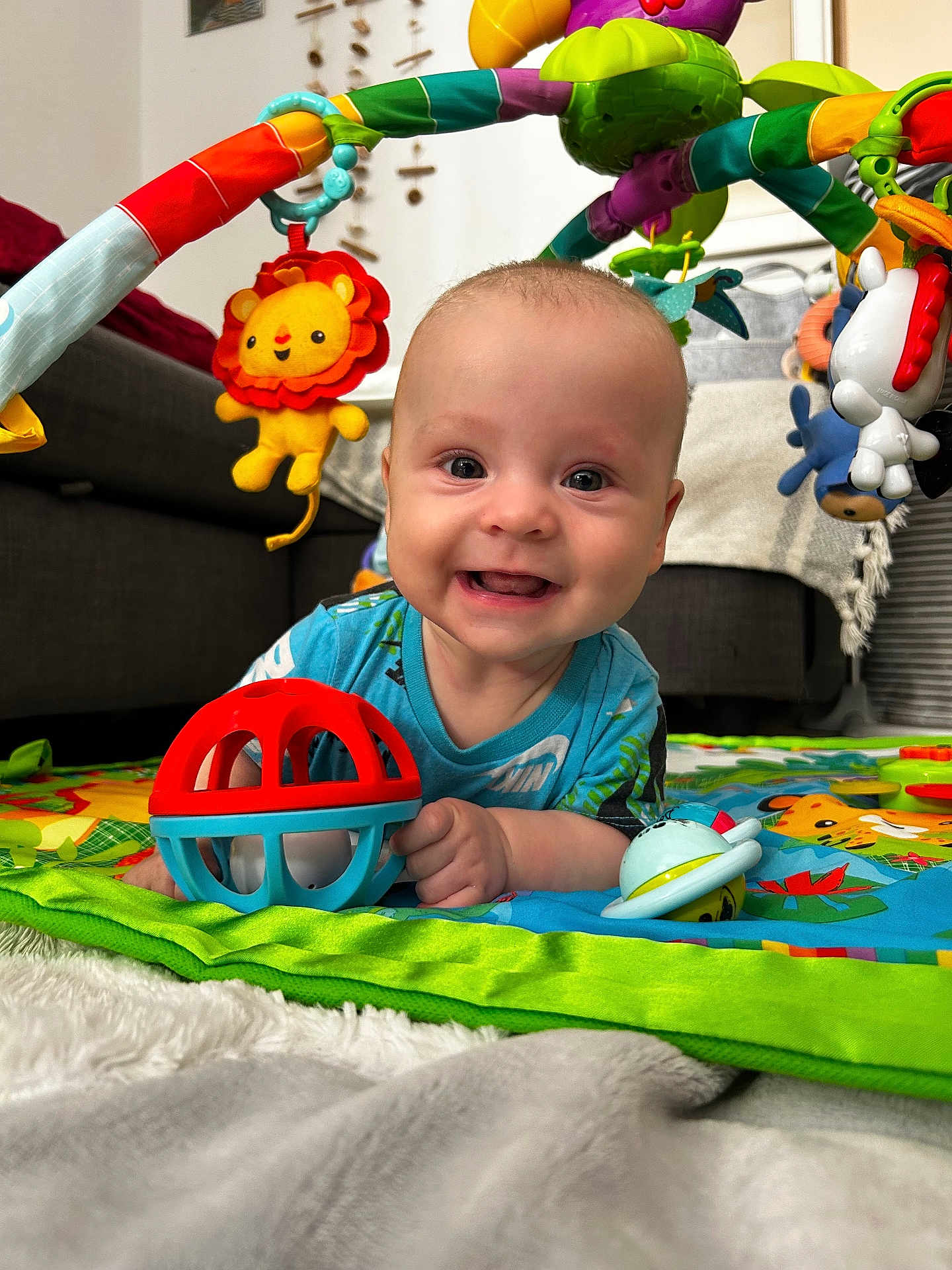 Gioele participe au concours pour gagner de l'argent avec cette photo : baby, smiling, toy, play_mat, indoor, child, colorful, plush_toy, happy, crawling, living_room, fabric, person, cute, infant, play_gym, face, blue_shirt, carpet, close_up