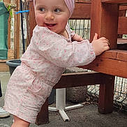 Rose a rejoint le concours — aidez-le/la à gagner de superbes lots ! toddler, child, baby, pink_bow, headband, shoes, socks, outdoor, bench, wooden_furniture, smiling, clothing, garden, plants, fence, concrete, happy, person, cute, exploring